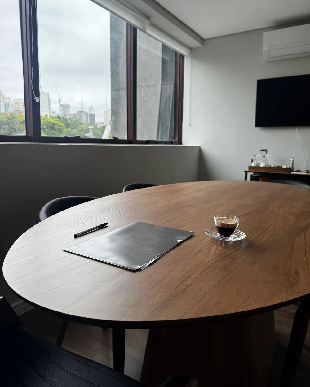 Sala de reunião do escritório, com mesa de madeira, café servido e vista da cidade